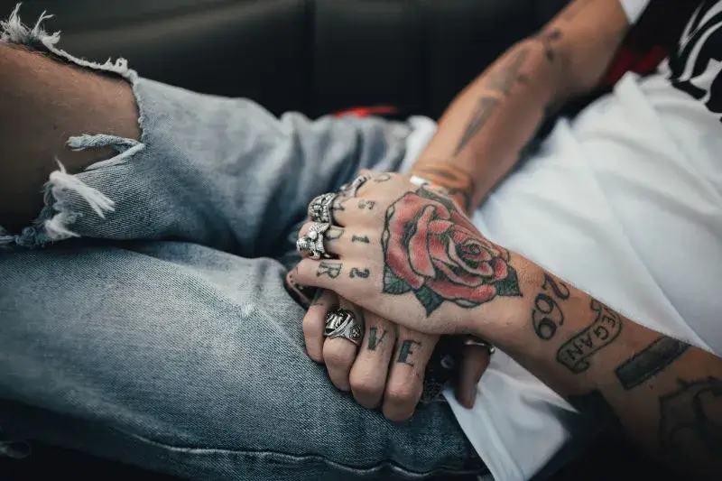 A rose-tattooed person crossing hands in their lap.
